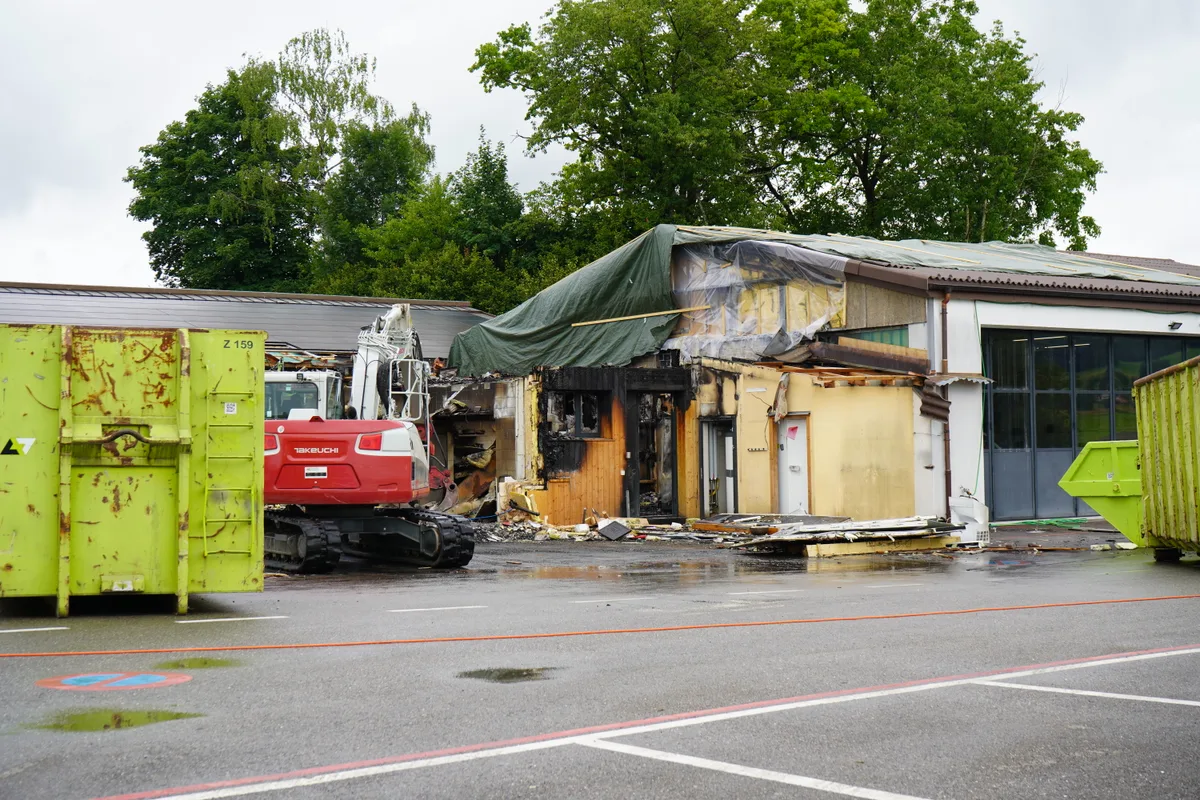 Ein abgebranntes Haus, davor ein Bagger, der aufräumt.